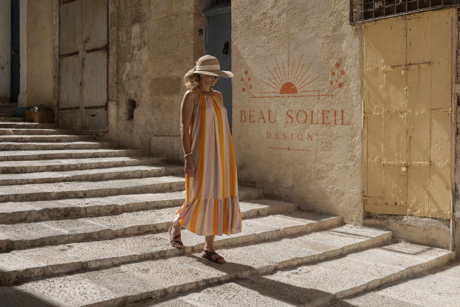 Femme en robe rayée colorée descendant des marches en pierre, logo Beau Soleil Design sur le mur